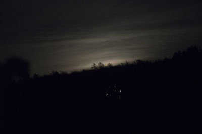 Silhouette trees on landscape against sky at night