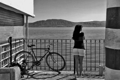 Man with bicycle on railing by sea against sky