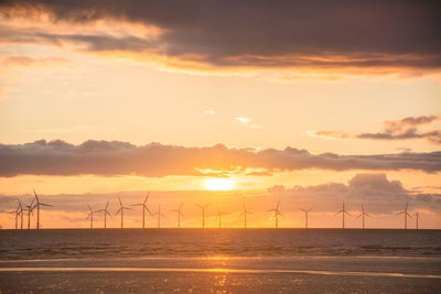 Wind turbines on land against sky during sunset