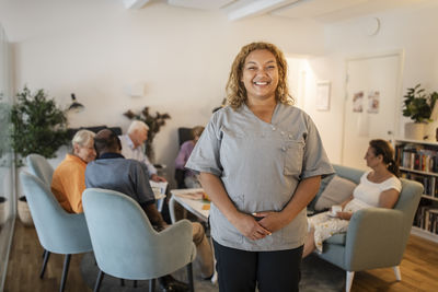 Portrait of smiling female nurse standing with hands clasped at nursing home