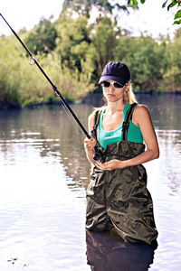 Mid adult woman wearing sunglasses fishing while standing in lake