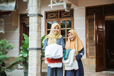 Smiling mother and daughter holding clothes standing outdoors