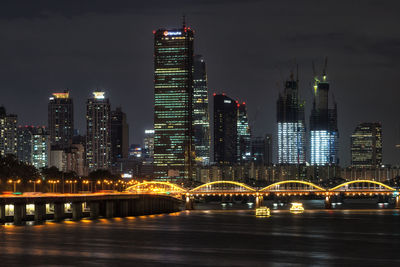 Illuminated bridge and buildings against sky at night