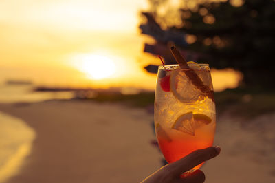 Close-up of hand holding drink against orange sky