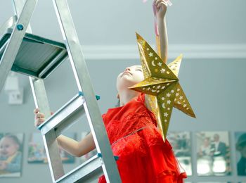 A little girl in a festive red dress is busy decorating the room with a paper gold star. new year 