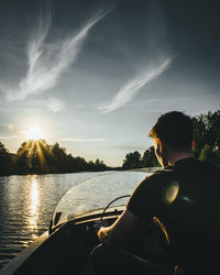 Rear view of man riding speedboat against sky during sunset