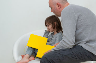 Midsection of father holding baby while sitting against wall