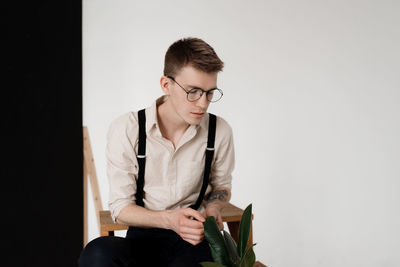 Young man with plant sitting against white background