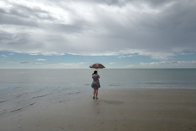 Rear view of woman with umbrella walking at beach