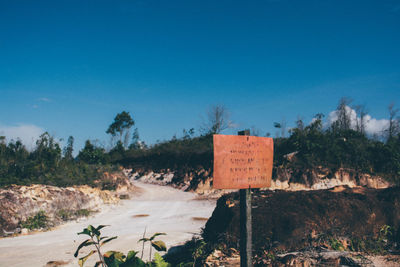 Road sign by trees against clear blue sky