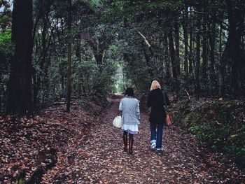 Rear view of women walking on road against trees