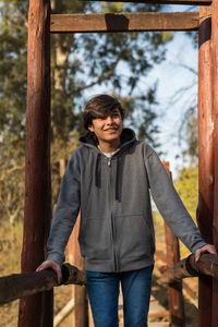 Portrait of young man standing on railing against trees