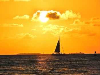 Silhouette sailboat sailing on sea against orange sky