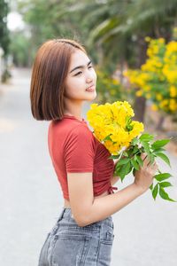 Young woman holding yellow while standing by flower
