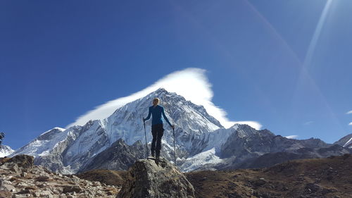 Rear view of man standing on snowcapped mountain against blue sky