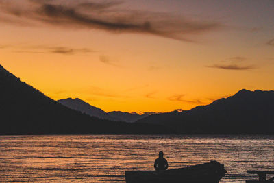 Silhouette people sitting on mountain against orange sky