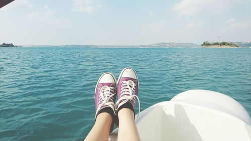 Close-up of feet with sport shoes against sea