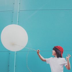 Boy playing with balloon while standing against wall