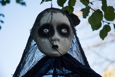 Low angle view of spooky sculpture hanging from tree against sky during halloween