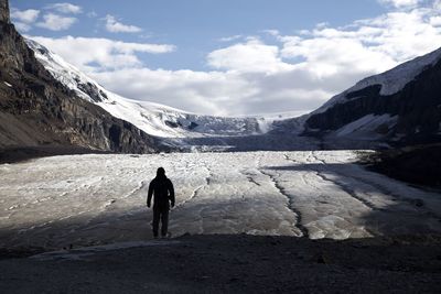 Rear view of person hiking on snowcapped mountain against sky