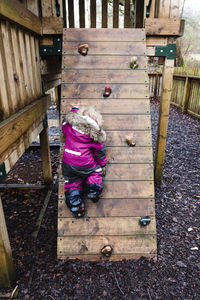 Rear view of girl rock climbing at park during rainy season