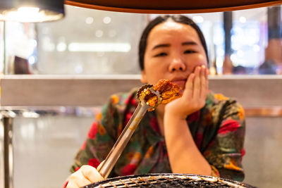 Portrait of woman holding food by barbecue grill in restaurant