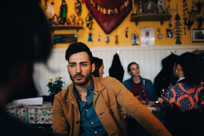 Young man looking at friend while sitting against women in restaurant during brunch