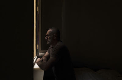 Adult man looking through window in room