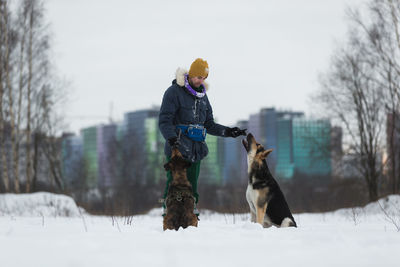 Man playing with dogs on snow covered land against sky