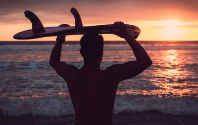 Silhouette man with arms raised on beach against sky during sunset