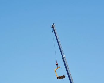 Low angle view of crane against clear blue sky