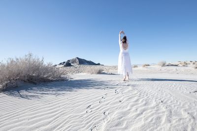 Woman with umbrella on sand against clear sky