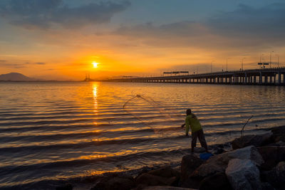 Scenic view of sea against sky during sunset with a lone fisherman