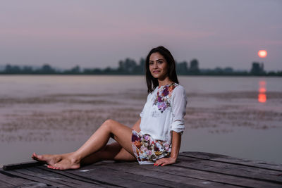 Portrait of woman sitting on pier over lake against sky