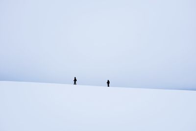 Low angle view of people walking on snow covered landscape against clear sky