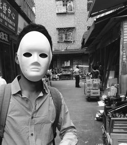 Man wearing mask standing on street against buildings in city