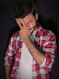 Portrait of young man standing against black background