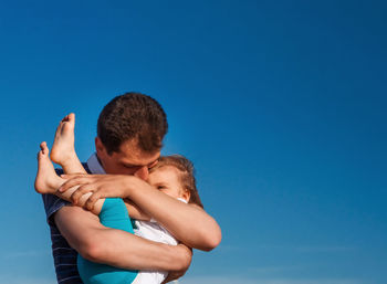 Father embracing daughter against blue sky