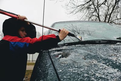 Boy cleaning snow from car windshield during winter