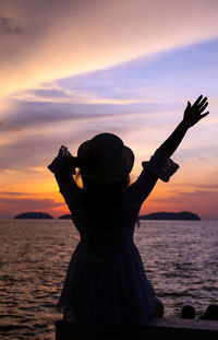 Rear view of silhouette man holding sea against sky during sunset