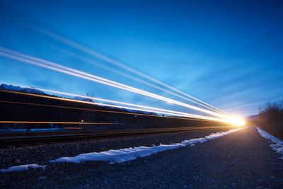 Light trails on road against blue sky at night during winter