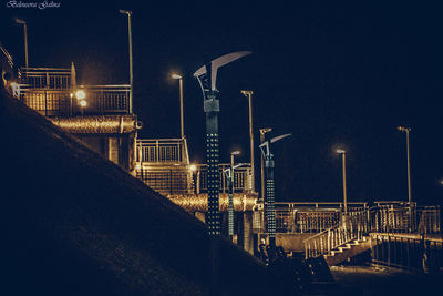 Illuminated factory by sea against clear sky at night