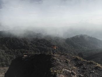 Rear view of woman standing on mountain against sky in foggy weather