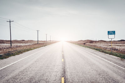 Scenic view of road amidst fields against sky