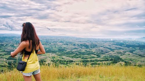 Rear view of young woman standing on landscape against sky