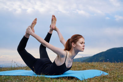 Side view of young woman doing yoga at beach against sky
