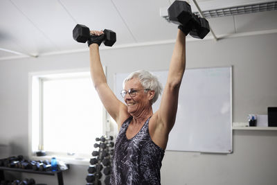 Happy senior woman exercising with dumbbells at health club