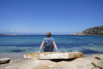 Rear view of man looking at sea against blue sky