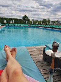 Low section of man relaxing in swimming pool against sky