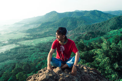 Full length of man sitting on cliff during sunny day